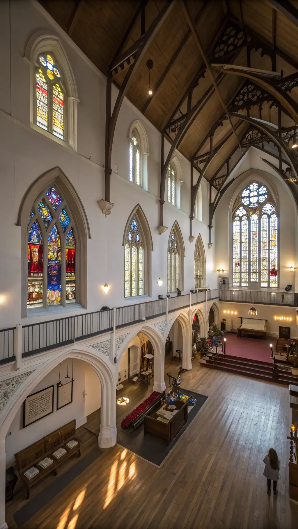 Loft inside converted Gothic church with 50ft nave, original stained glass windows, white walls with rainbow light projections, floating mezzanine bedroom pod, industrial accents and restored ecclesiastical details, shot with a tilt-shift lens.