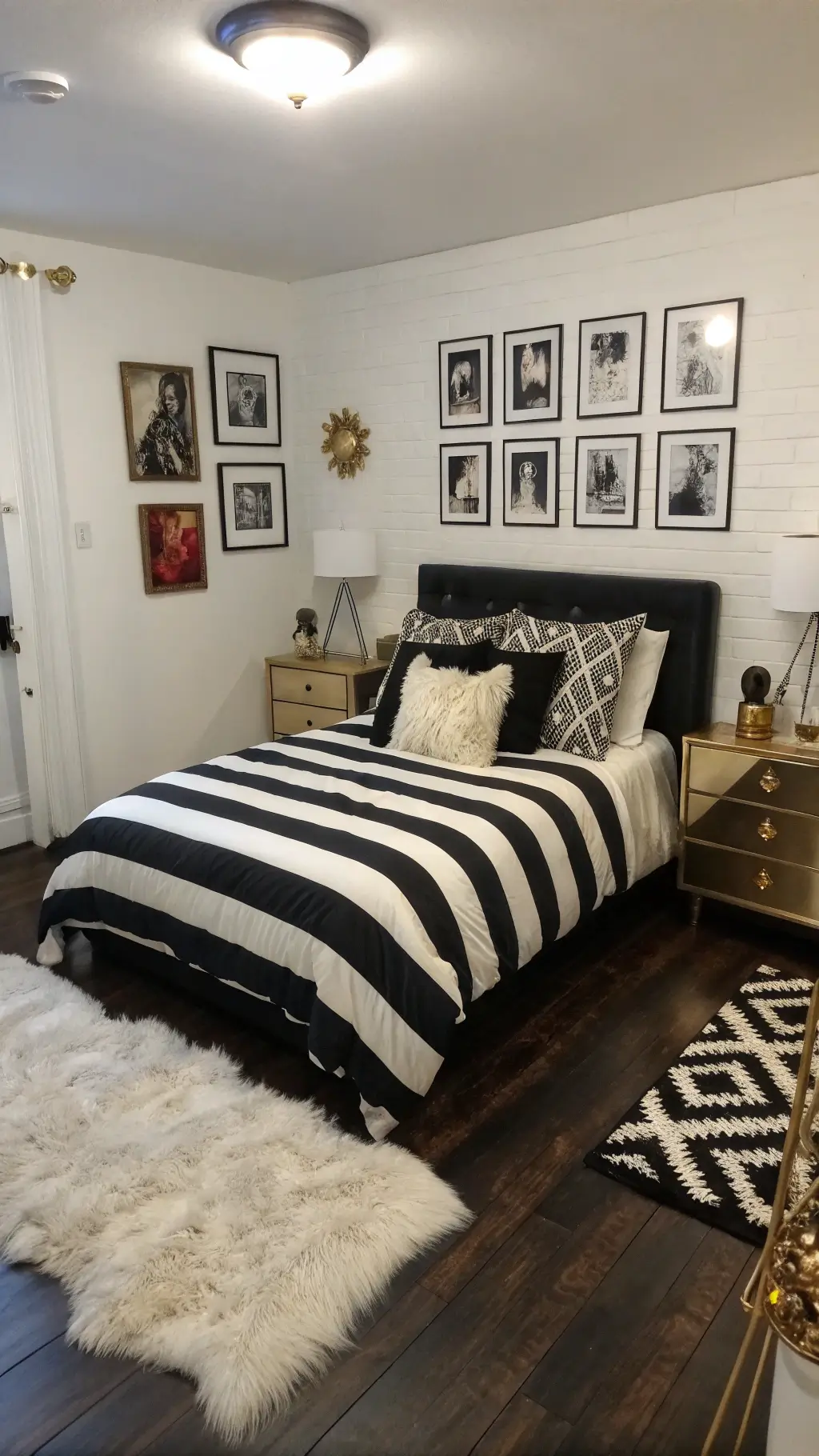 Maximalist urban bedroom with white walls adorned with black and white photography, a queen bed with bold striped duvet, mixed pattern pillows, lucite nightstands with black accessories, over a layered white faux fur rug and black hardwood floor with brass details.