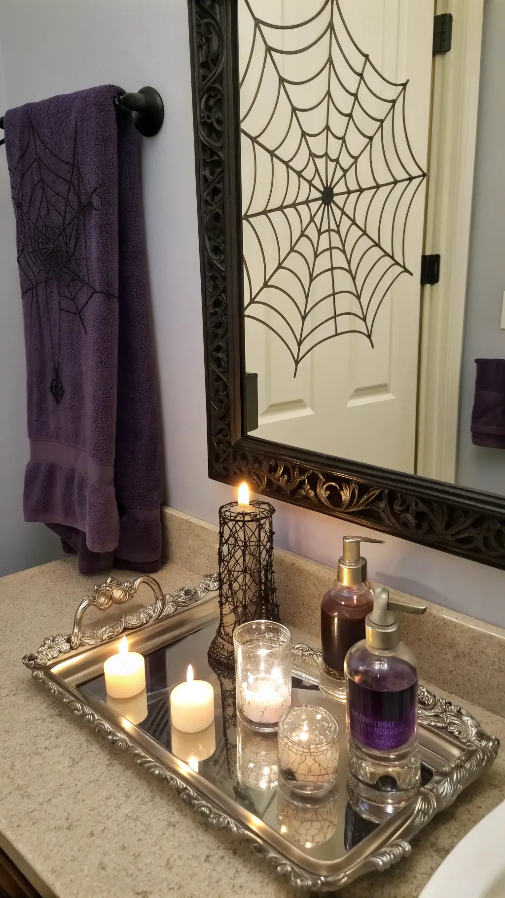 Bathroom vanity reflection showcasing antique silver tray with potion bottles, crystal balls on black lace spider web overlay, LED candles, purple hand towels and mercury glass accessories, lit by a ring light
