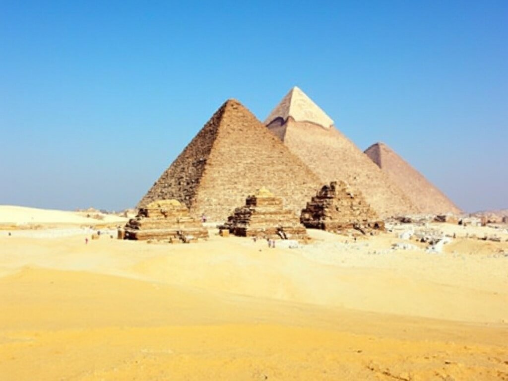 Three pyramids of Giza against a clear blue sky, surrounded by vast golden sand